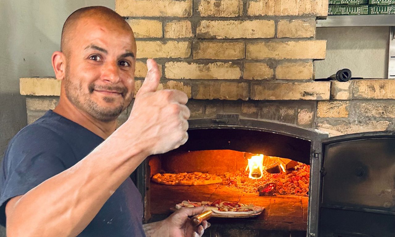 Leende man står framför en pizzaugn påväg att tillaga en pizza