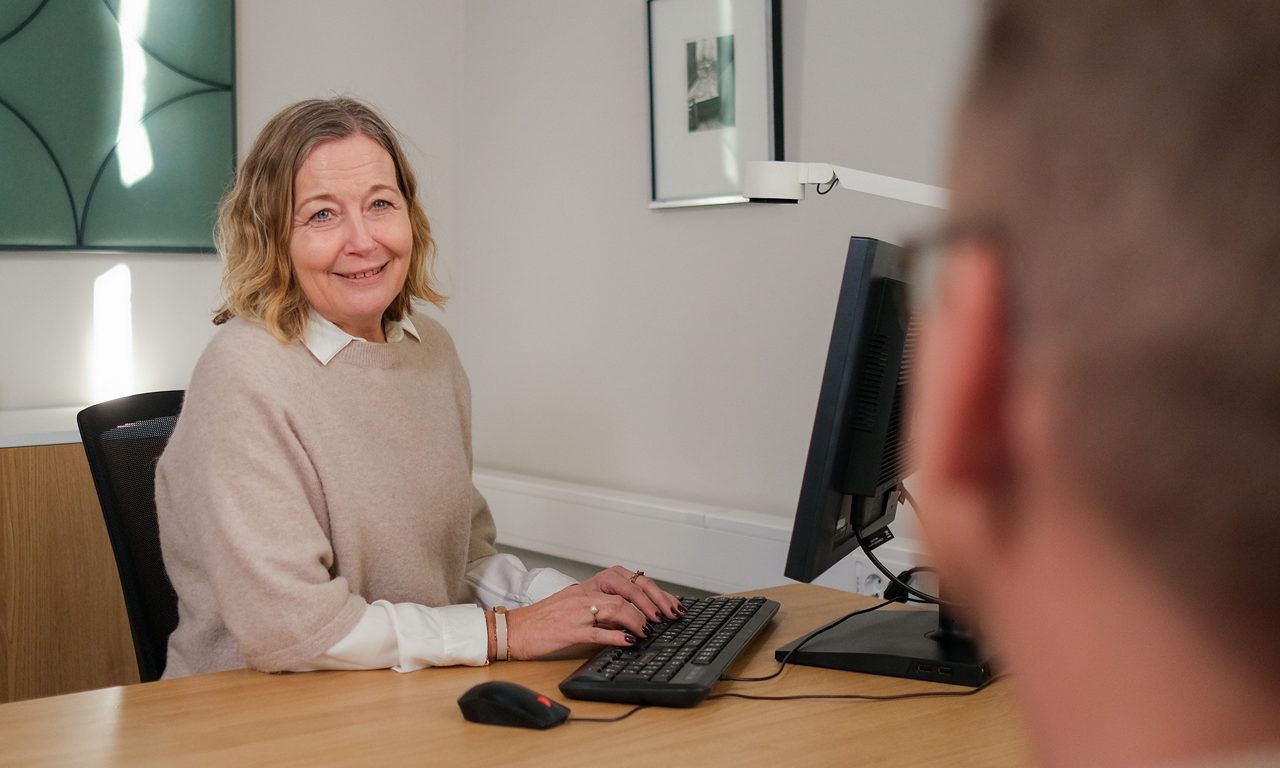 Rådgivningsmöte i kontorsmiljö. En kvinna sitter vid sitt srkivbord och samtalar med en kund.