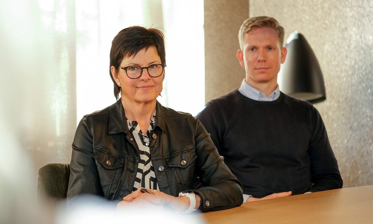 En kvinnlig och en manlig rådgivare sitter vid ett bord och ser in i kameran