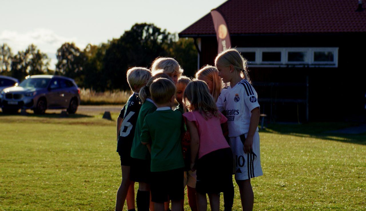 Barn står i samlad grupp på fotbollsplan