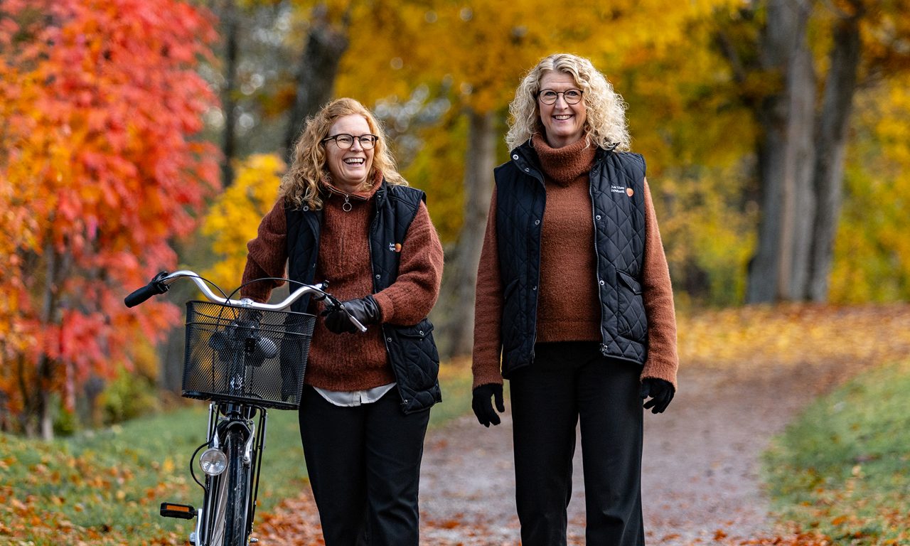 Två kvinnor med en cykel med höstlöv utomhus