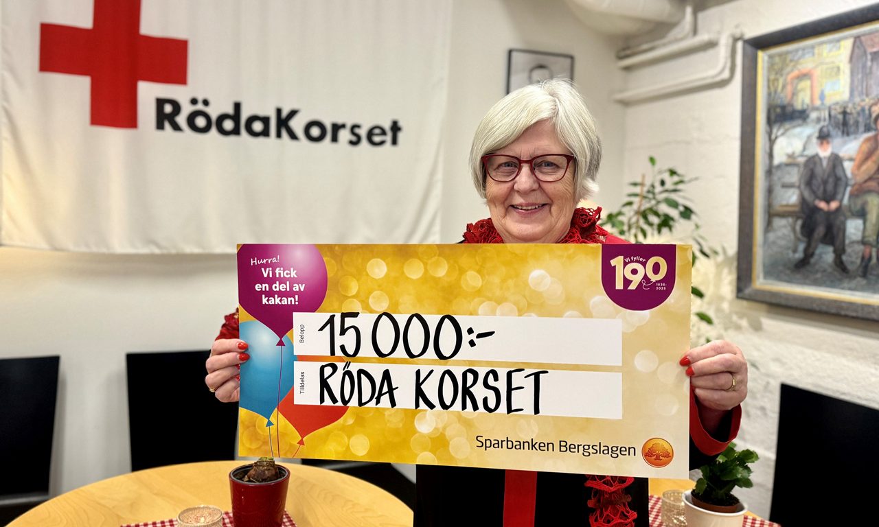 En kvinna från Röda Korset håller upp deras värdecheck på 15 000 kr.