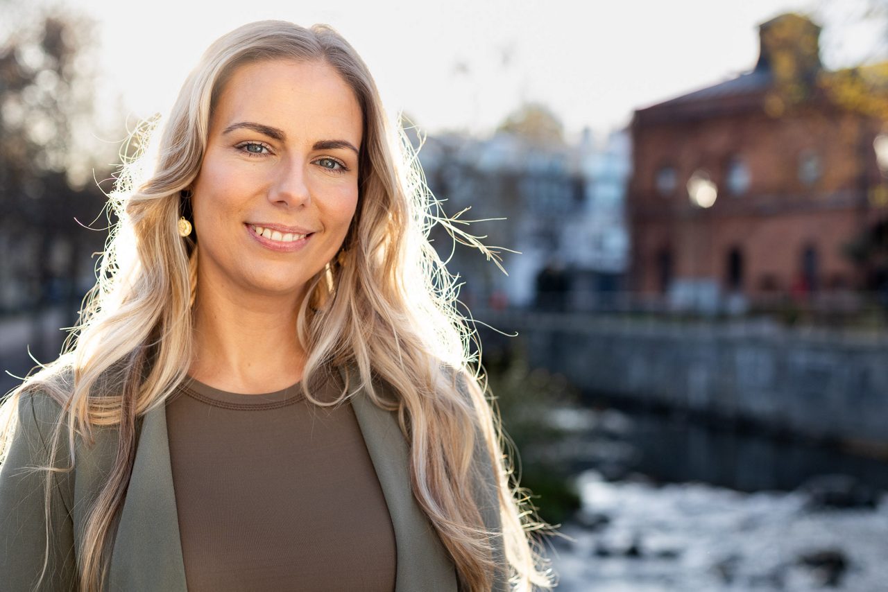 Bolånerådgivare står utomhus i stadsmiljö och ler mot kameran