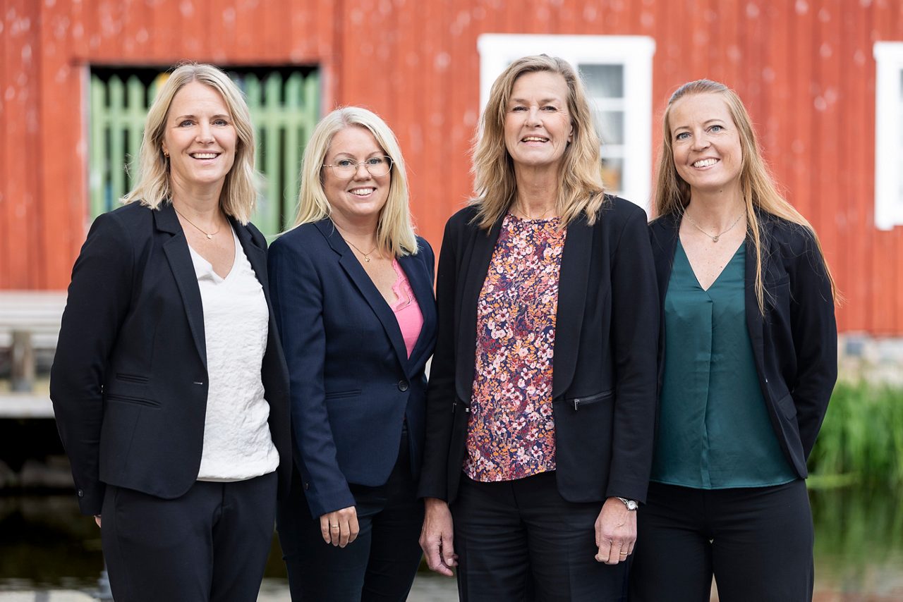 Roslagens Sparbanks premiumrådgivare samlade framför en röd träbyggnad i bankens lokala miljö. Teamet arbetar nära kunderna för att ge personlig rådgivning och skräddarsydda lösningar inom sparande, lån och investeringar. På bilden står de tillsammans, klädda i kavajer och med ett professionellt och välkomnande uttryck.