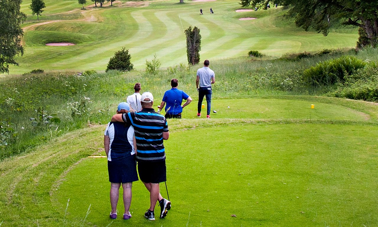 Personer står och väntar på att slå ut på en golfbana.