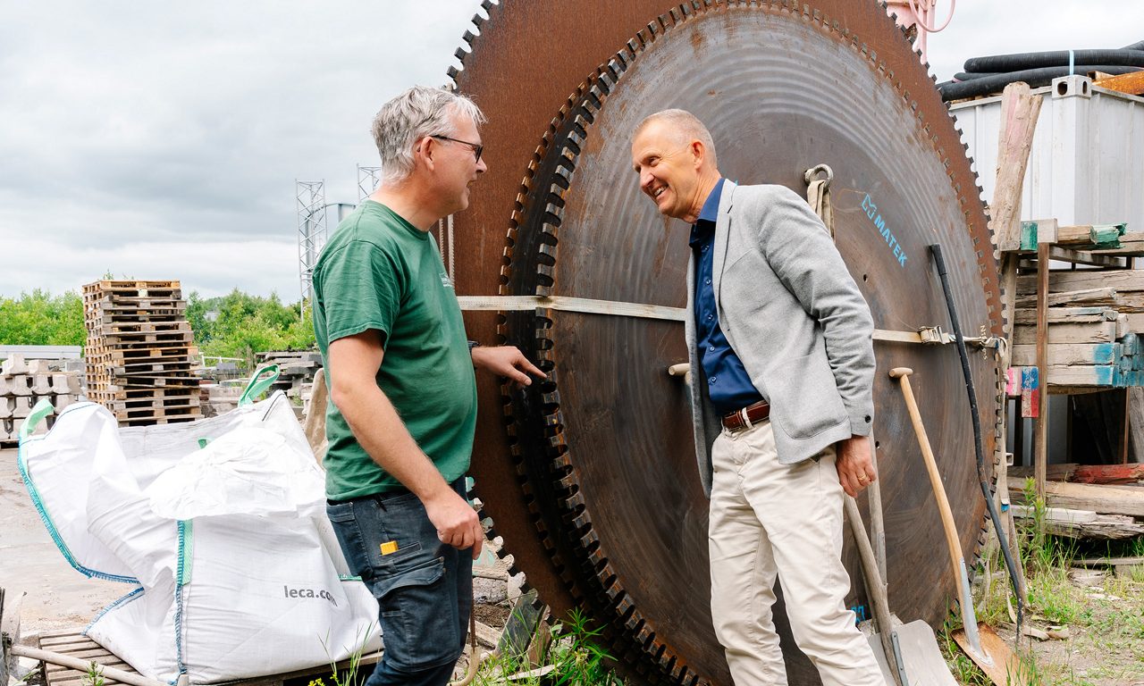 Niklas och Henric samtalar ute på gården med en giganstisk sågklinga i bakgrunden