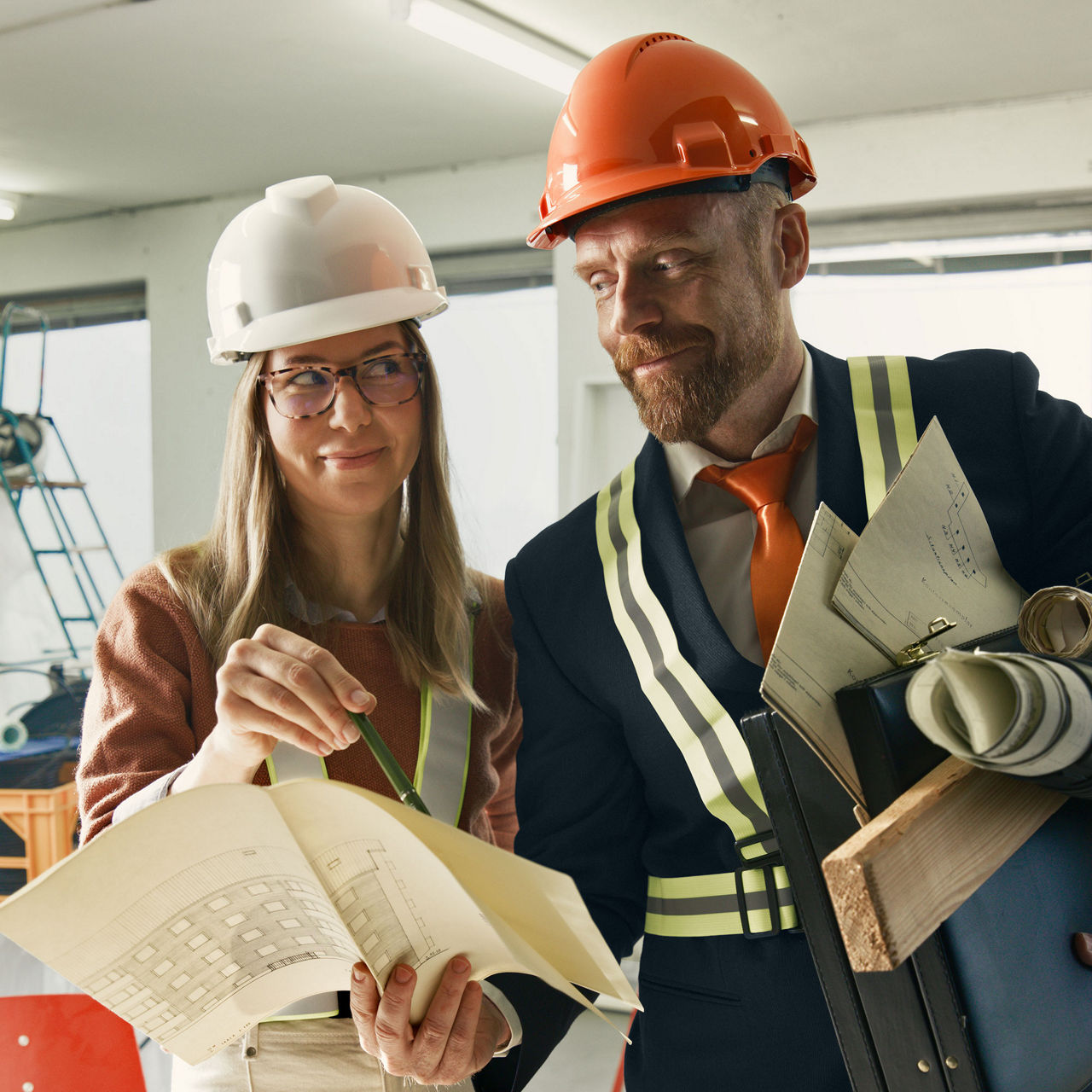 Två arkitekter diskuterar ritningar på en byggarbetsplats.