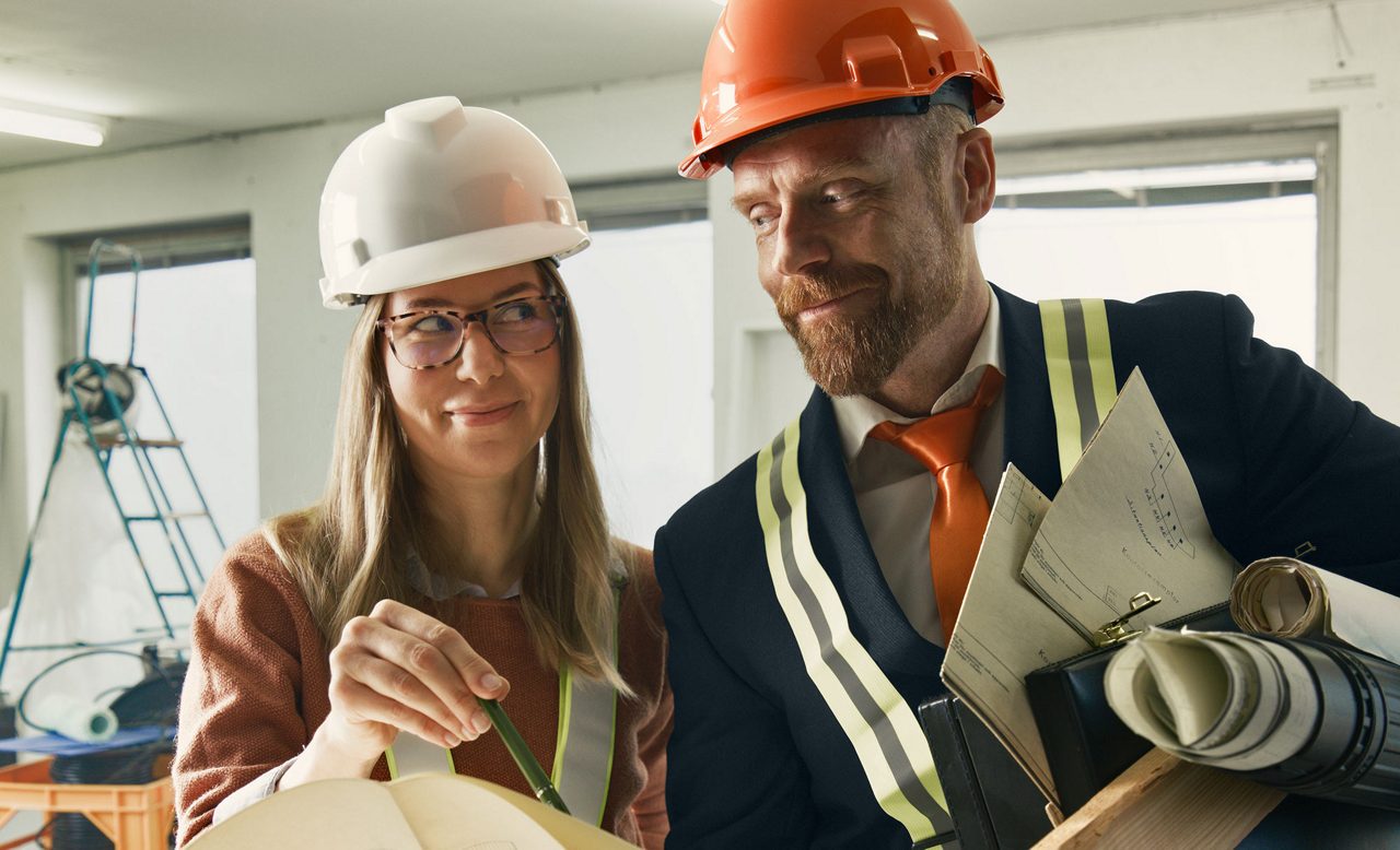 Två arkitekter diskuterar ritningar på en byggarbetsplats.