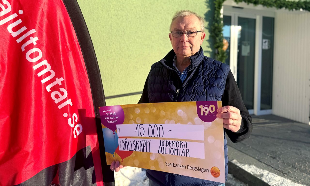 Äldre man från Sällskapet Hedemora jultomtar som håller i en värdecheck .