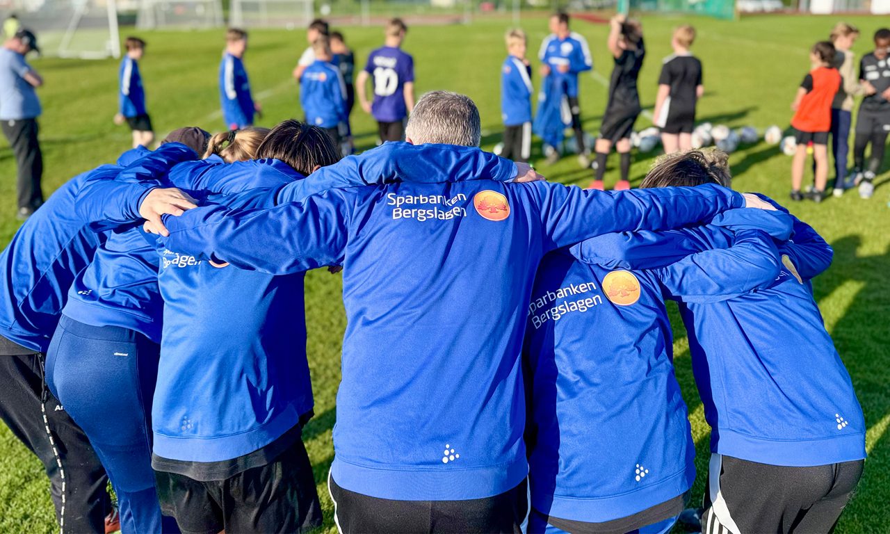Fotbollsspelarna håller om varandras axlar och man ser deras ryggtavlor.
