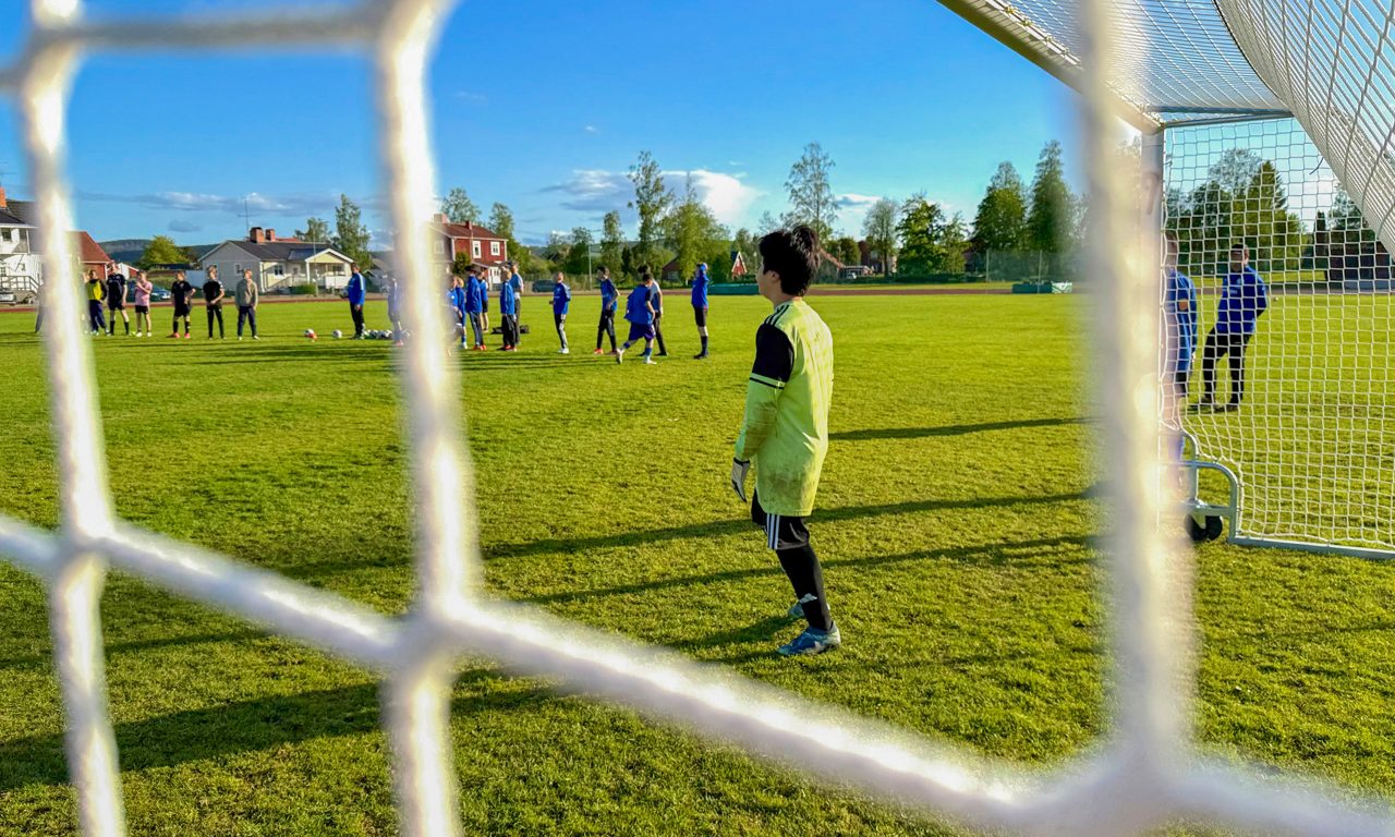 Närbild på målnätet med målvakt samt fotbollsspelare i bakgrunden.