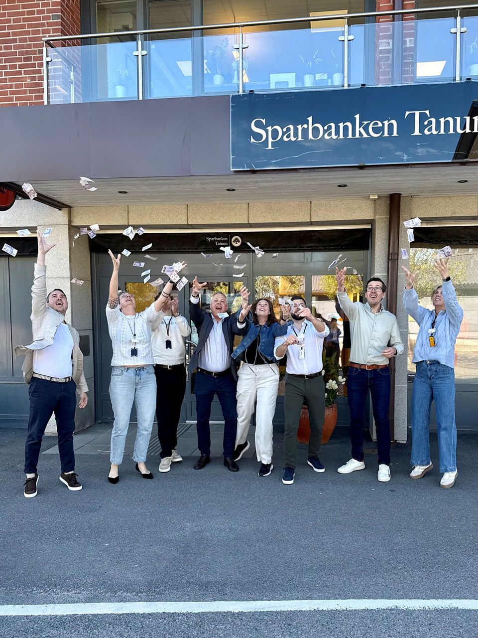 Gruppbild över några i personalen på Sparbanken Tanum som kastar pengar i luften