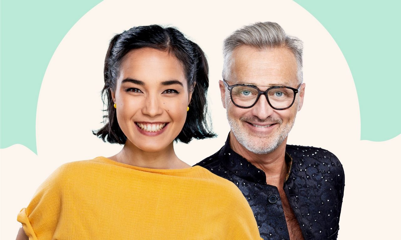 Leende kvinna i gul tröja och man i svart skjorta poserar framför ljus bakgrund.