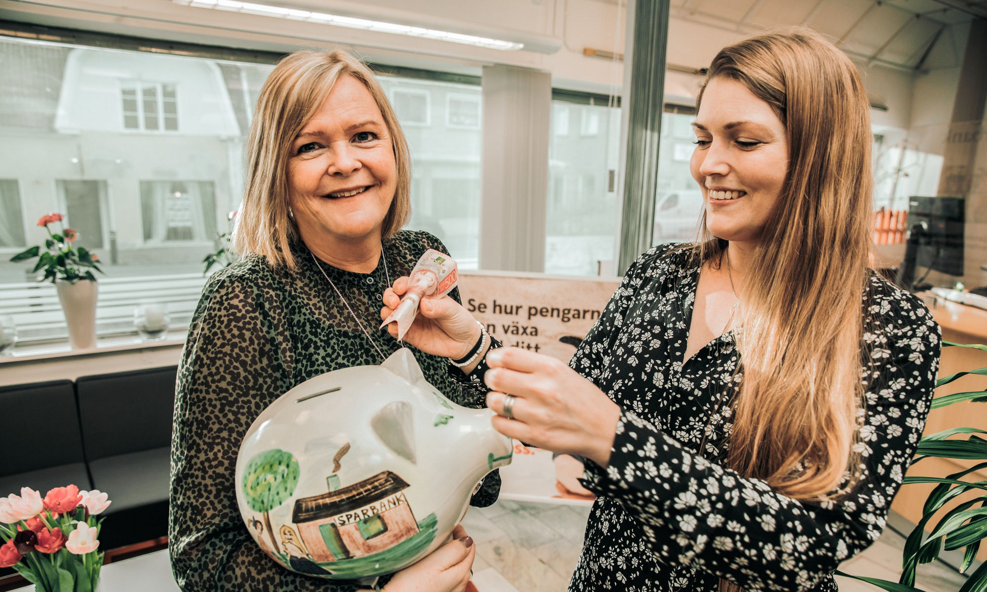 Två kvinnor som håller en spargris emellan sig