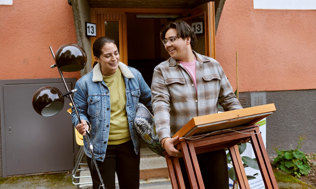 En medelålderskvinna hjälper en yngre kille att flytta. Båda två bär på möbler.