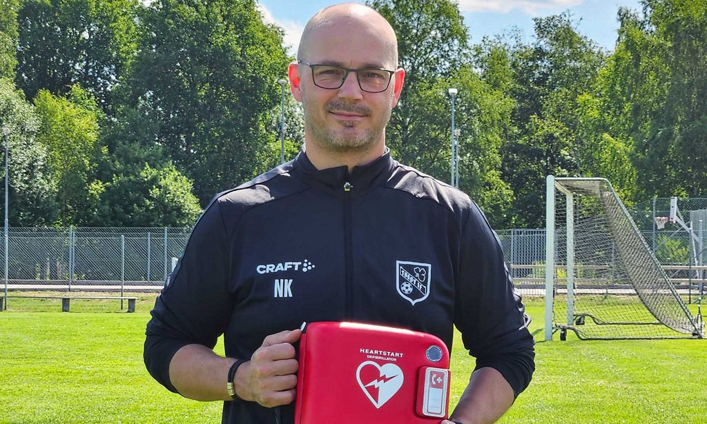 En man på en fotbollsplan från föreningen Treby IF håller en hjärtstarare i händerna.