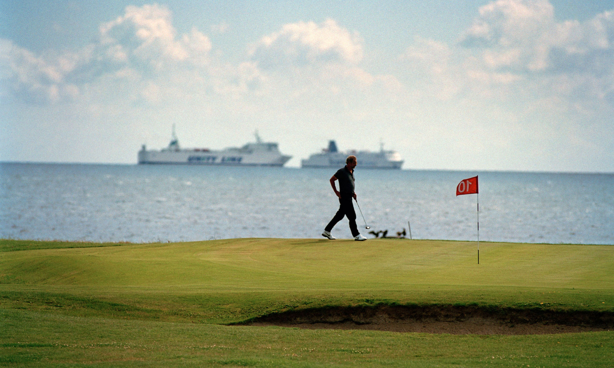 Man spelar golf med havet i bakgrunden
