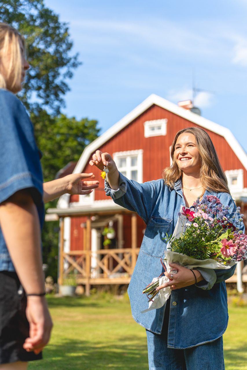 En kvinna håller i en blombukett och ger nycklar till en annan kvinna