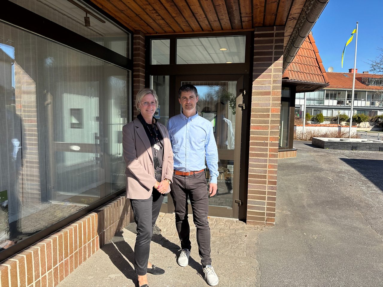 Anna och Tobias står utanför banken och ler mot kameran