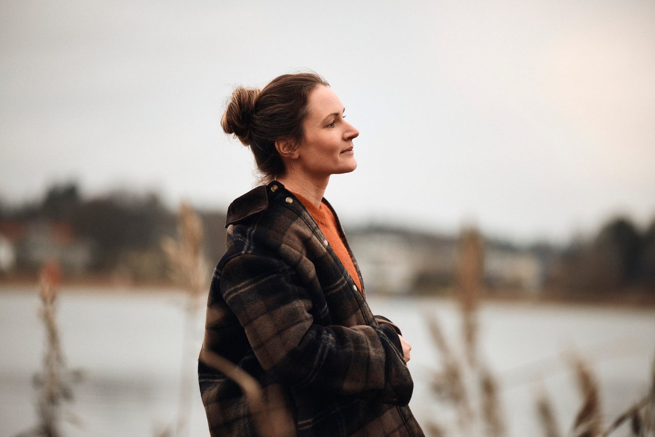 En person i ytterkläder står vid en sjö eller vik och ser ut över vattnet i ett lugnt landskap.