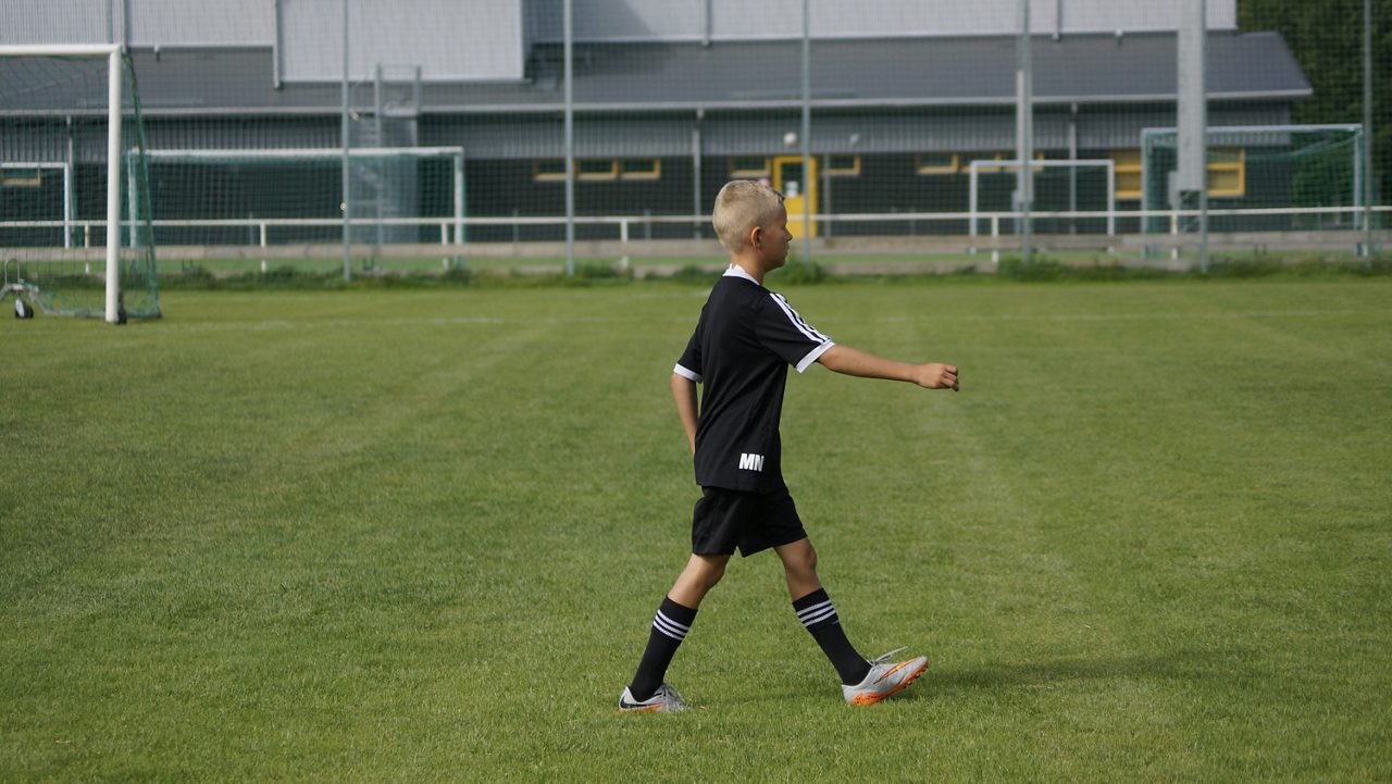 Barn i svarta fobollskläder skjuter en boll  mot mål