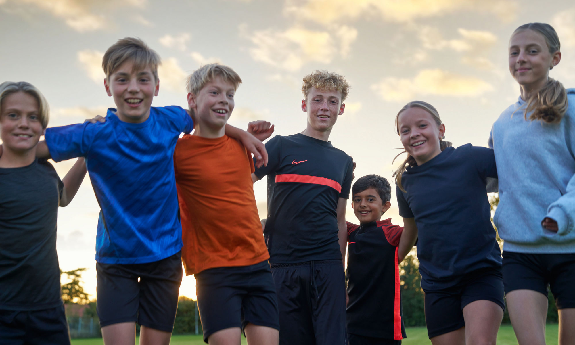 Sju barn och unga håller om varandra och ler. 