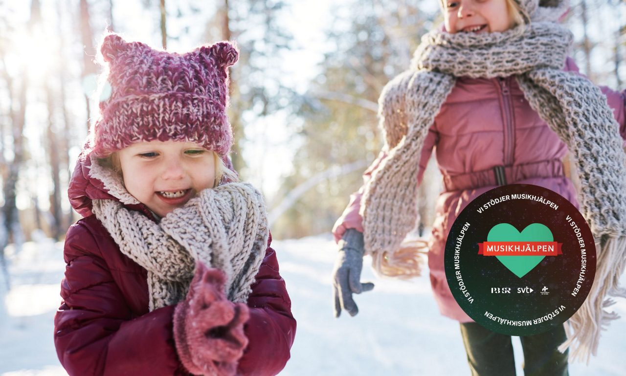 Två tjejer leker i snön tillsammans med logotypen för Musikhjälpen.