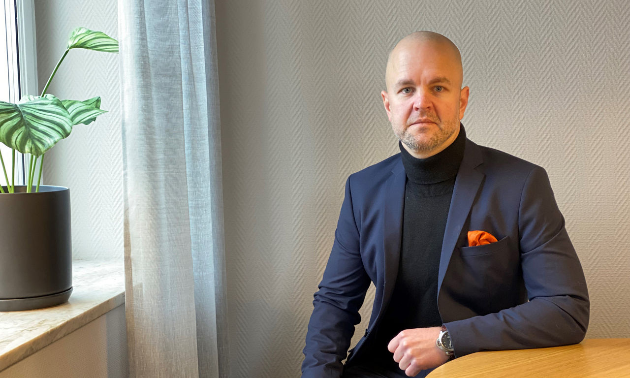 man i svart polo och blå kavaj tittar in i kameran