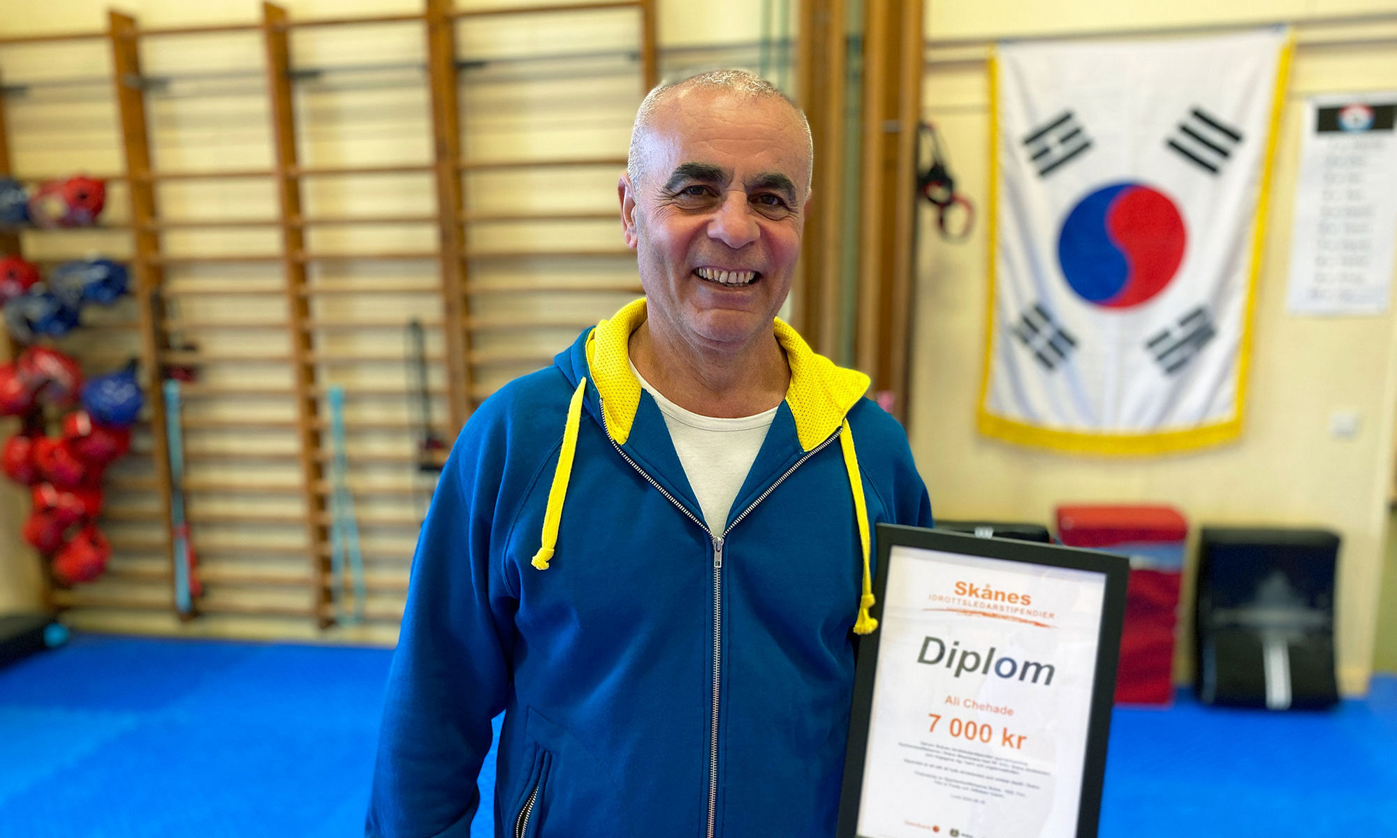 Taekwondotränare i en träningshall håller upp sitt Idrottsledarstipendium. 