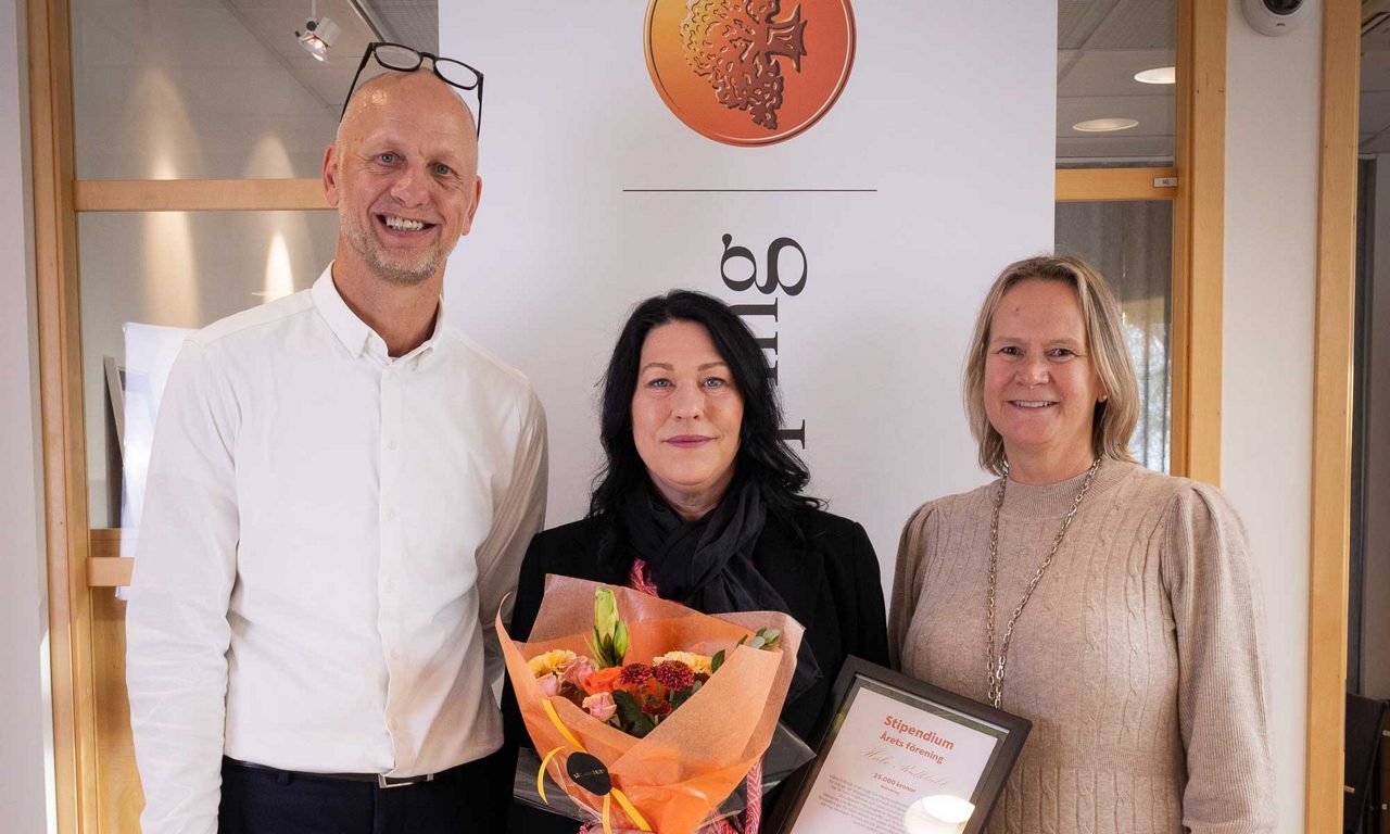 Tre personer som tittar mot kameran. Hon i mitten håller en blombukett samt ett stipendium