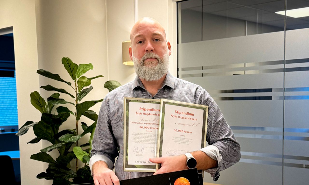 en man håller två inramade stipendier