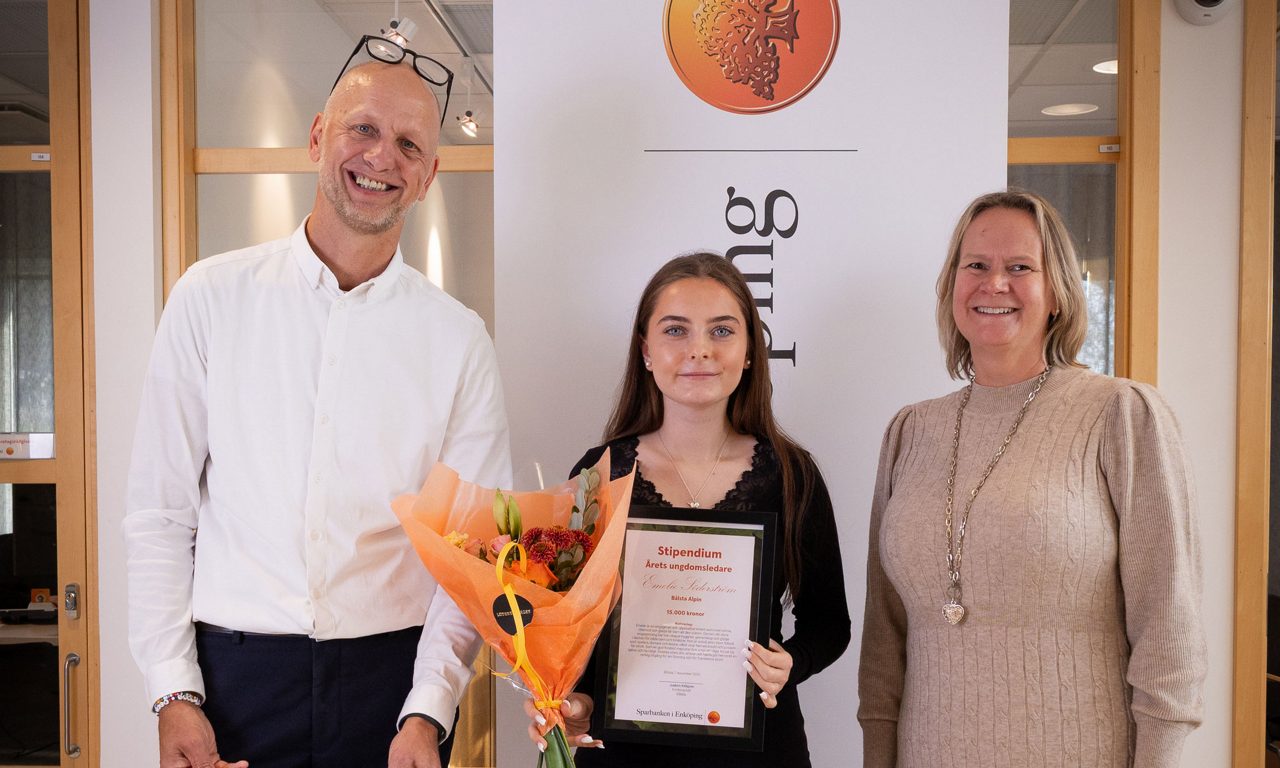 en man och två kvinnor. kvinnan i mitten håller en stor check, blombukett samt ett inramat diplom