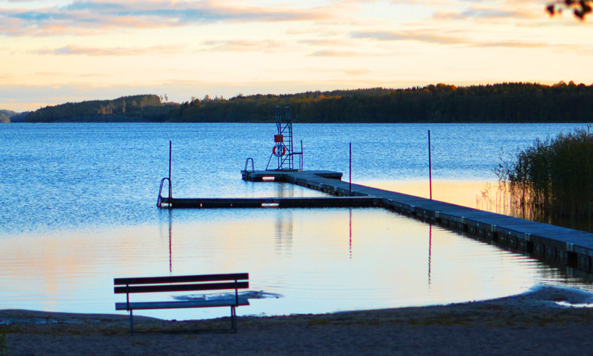 Solnedgång över sjö och badplats.