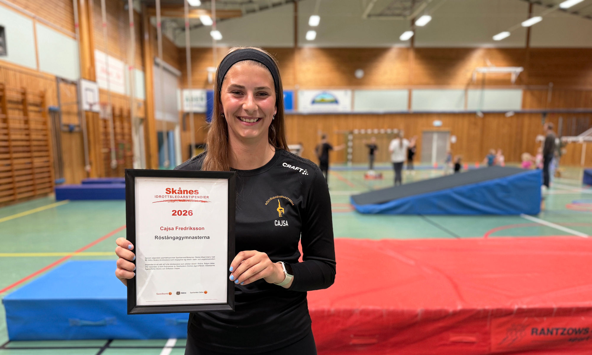 En ung kvinna håller ett diplom i en sporthall.