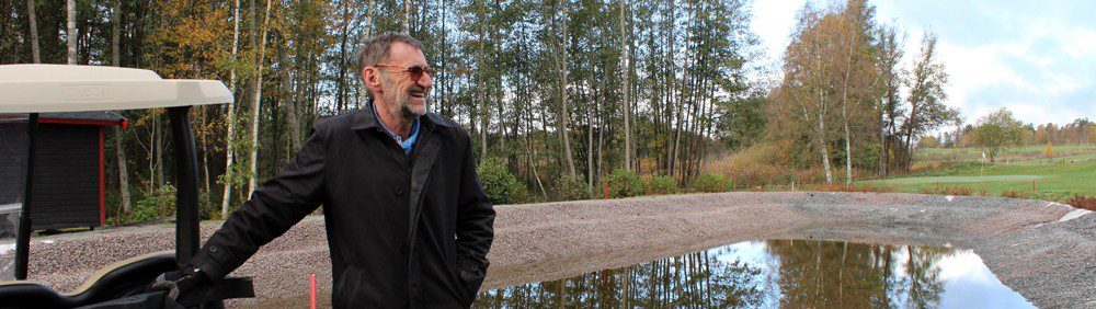 En man vid en golfbil framför ett vattenhål på en golfbana