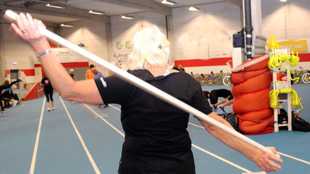 Äldre kvinna som tränar med en stång