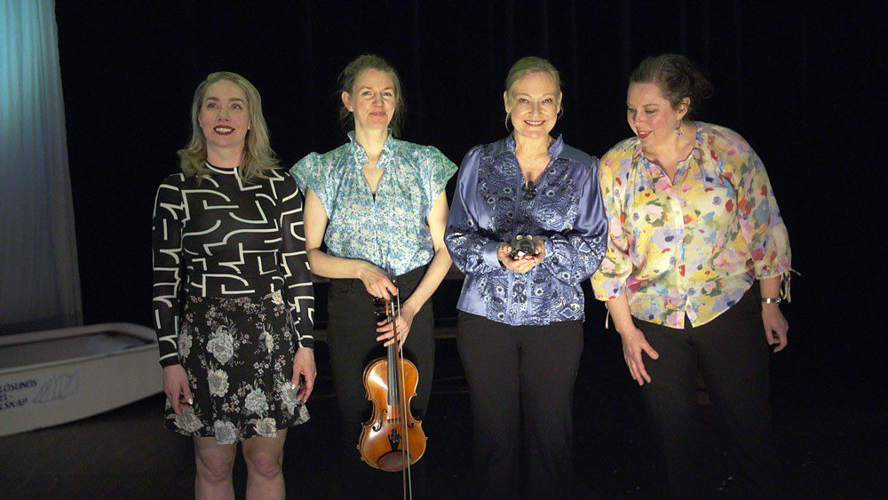 Fyra kvinnor på en mörk scen, en av dom håller i en fiol