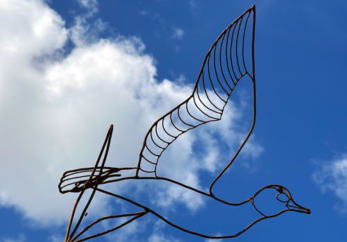 Skulptur av en fågel gjord av tjock ståltråd med himmeln i bakgrunden