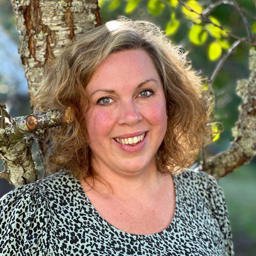 En leende kvinna lutar sig mot ett träd