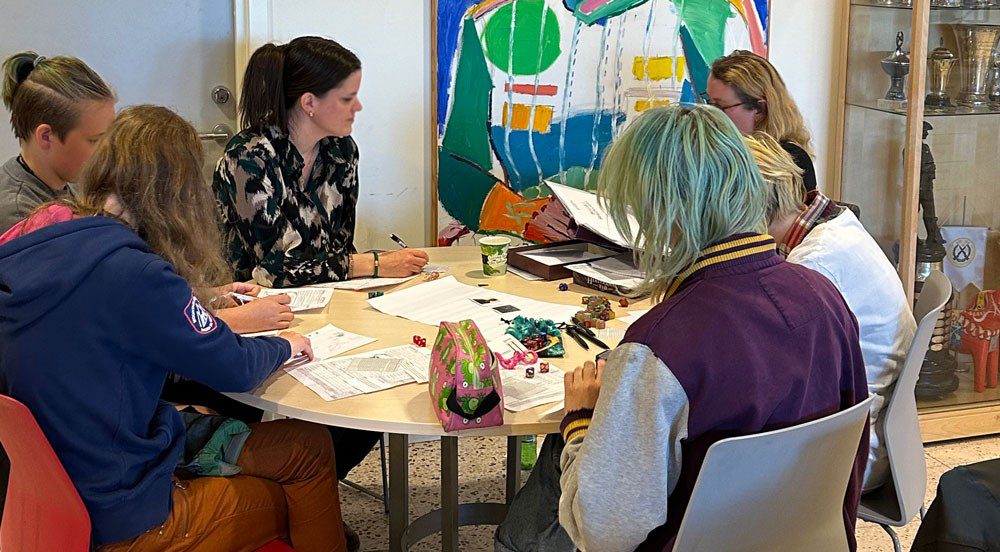 En grupp människor sitter runt ett bord med papper och tärningar