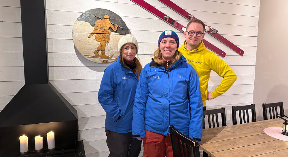 Tre personer i varma kläder framför skidor på en vägg