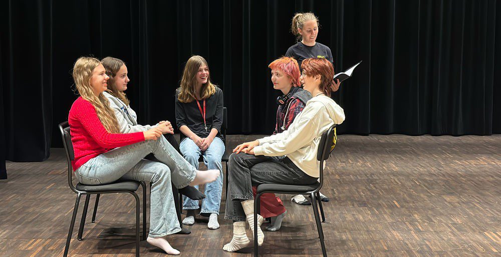 En liten grupp människor sitter på stolar i en cirkel i ett stort rum