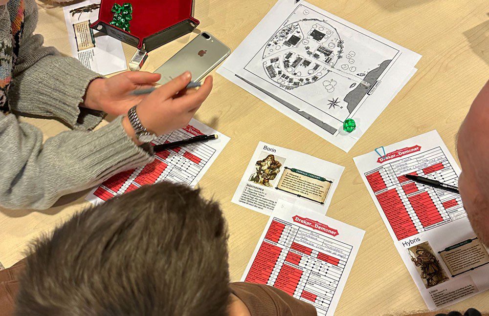 Personer sitter runt ett bord med spelformulär