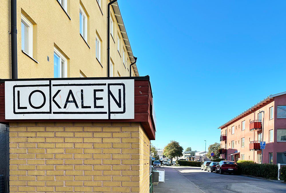 En väg med hus och en skylt för kulturhuset Lokalen
