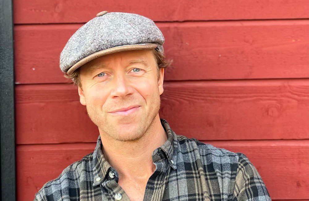 Leende man i keps framför en röd trävägg