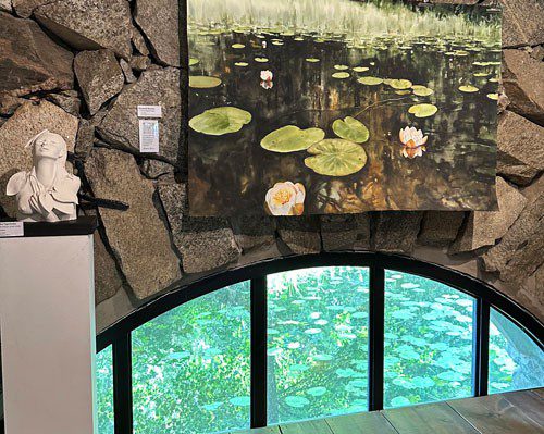 En målning av näckrosor ovanför ett fönster med en damm med näckrosor utanför