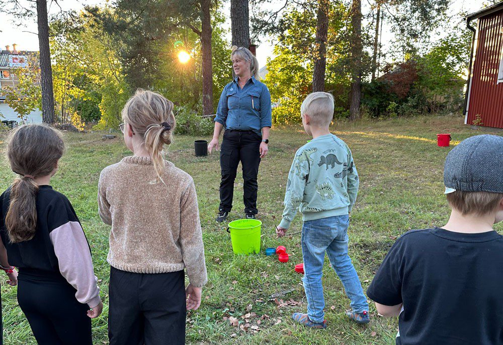 En kvinna förklarar en lek för barn utomhus