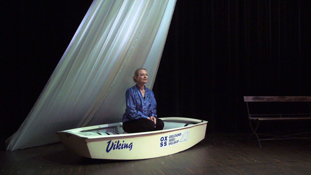 En kvinna sitter i en båt på en scen
