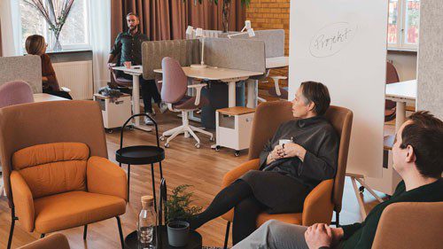 Två personer i fåtöljer och två personer vid skrivbord