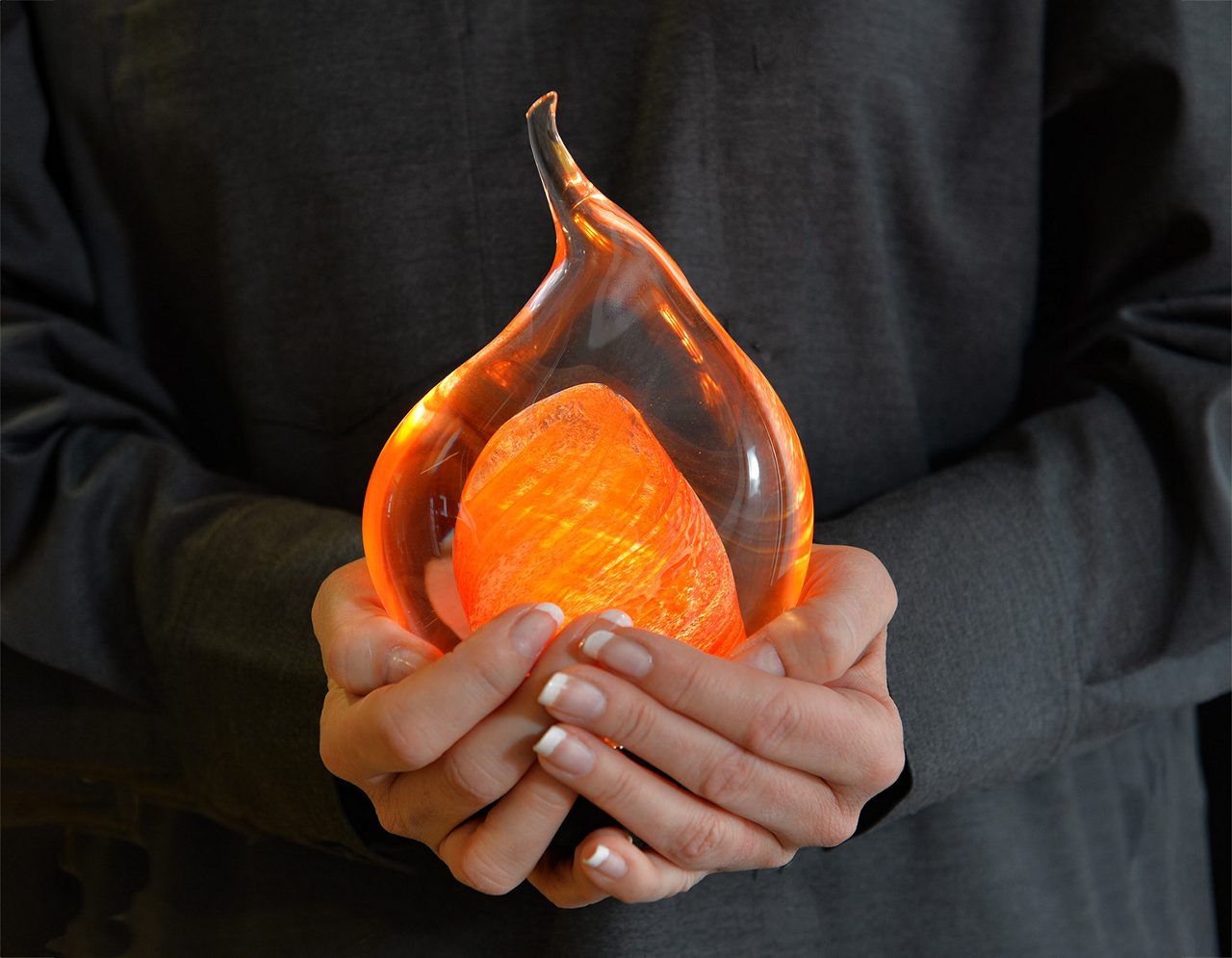 Two hands holds a lamp made in glass, shaped as a fire.